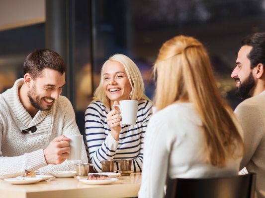 एक कैफे की मेज पर कॉफी पर बातें करते और मुस्कुराते हुए खुश दोस्त