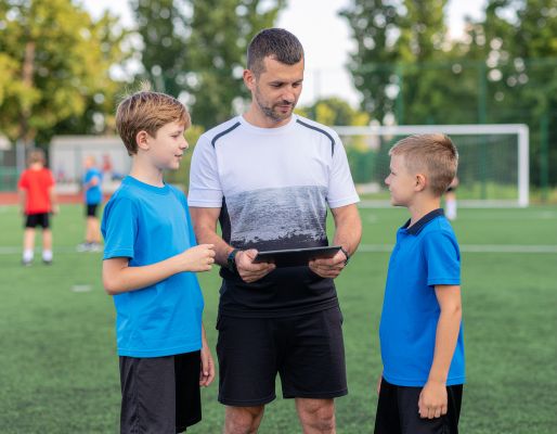Coach laat twee jongens een tablet zien en verkent daarmee een gepersonaliseerd verhaal of een leerapp.